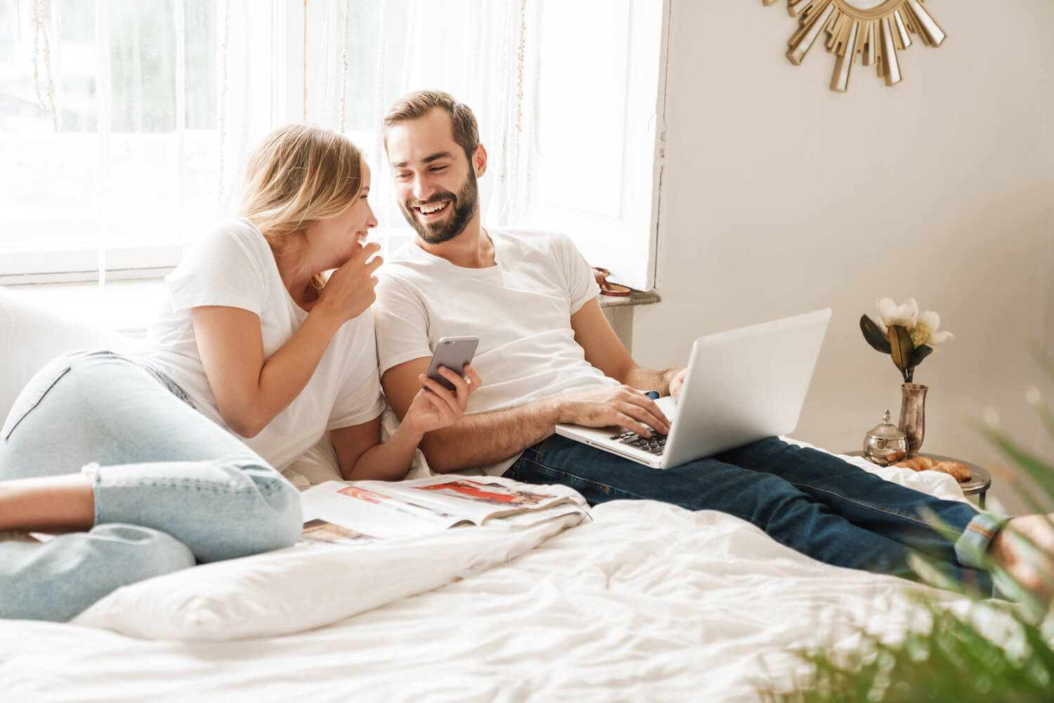 Couple sitting on bed with laptop smiling at each other