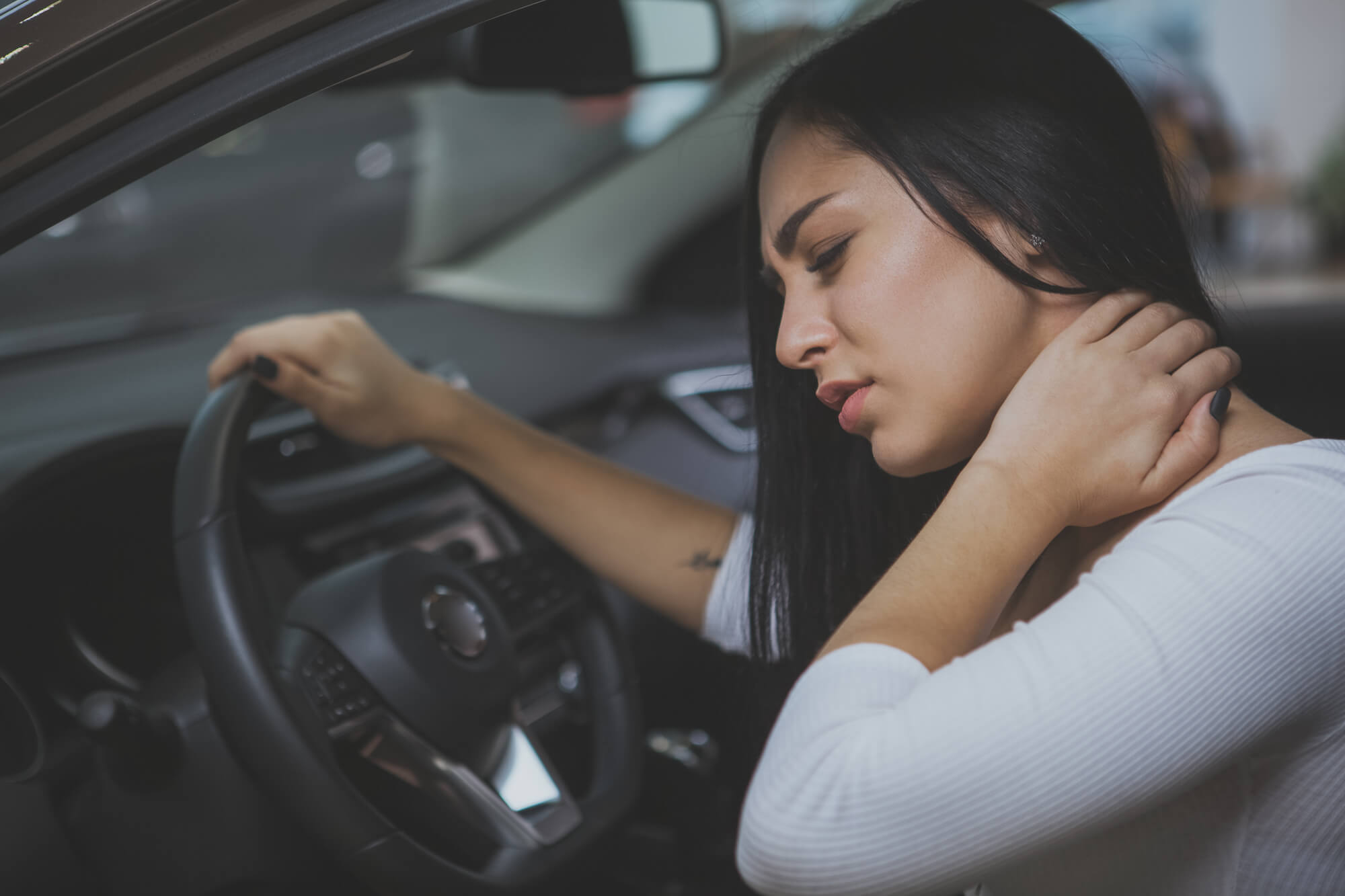 Young woman in vehicle holding back of her neck in discomfort